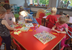 dzieci bawią się przy stolikach - układają wzory z koralików