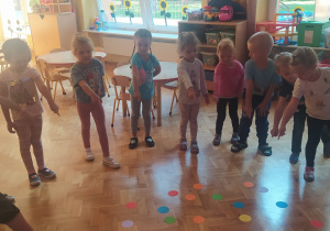 dzieci stoją w kole podczas zabawy z kolorowymi kropkami leżącymi na podłodze