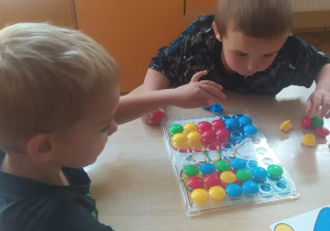 chłopcy przy stoliku układają motyla wg wzoru z wykorzystaniem kolorowych guziczków