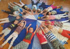 dzieci leżą na chuście animacyjnej z rękami wyciągniętymi nad głowami skierowanymi do środka chusty