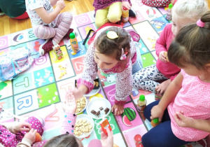 piknik w przedszkolu - dziewczynki częstują się słodyczami siedząc matach w sali