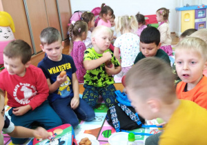 piknik w przedszkolu - chłopcy częstują się słodyczami siedząc matach w sali