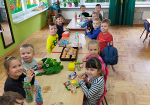 dzieci siedzą przy stolikach ze słodyczami a na środku blach z babeczkami