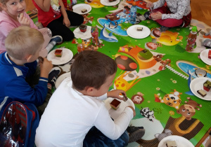 piknik w przedszkolu - dzieci siedzą w kole na macie i częstują się słodyczami siedząc na macie w sali