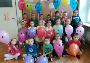 dzieci z grupy V pozują do zdjęcia z kolorowymi balonami i narysowanymi uśmiechniętymi buziami