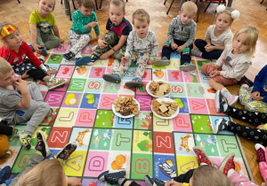 piknik w przedszkolu - dzieci z grupy VII częstują się słodyczami siedząc na macie w sali