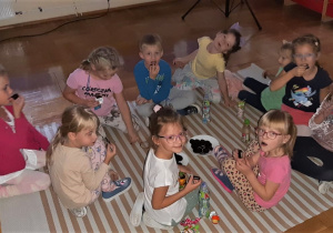 piknik w przedszkolu - dziewczynki z grupy III częstują się słodyczami siedząc na macie w sali