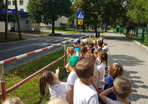 dzieci stoją na chodniku przy barierce i przyglądają się znakom drogowym - przejście dla pieszych szczególnie uczęszczane przez dzieci