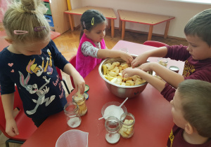 dzieci robią kompoty - wkładają pokrojone owoce do słoików z wsypanym cukrem