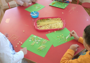dzieci na zielonych kartonach naklejają makaronowe obrazki