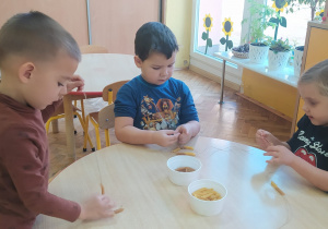 dzieci przy stoliku nawlekają makaron na sznurek