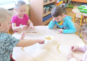 dzieci przy stoliku robią korale z makaronu