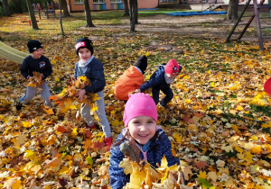 dzieci w ogrodzie przedszkolnym bawią się kolorowymi liśćmi