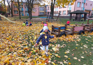dzieci w ogrodzie przedszkolnym siedzą i biegają po kolorowych liściach