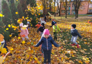 dzieci w ogrodzie przedszkolnym rzucają kolorowymi liśćmi