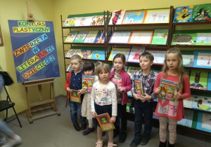 nagrodzona grupa dzieci w bibliotece stoi przed półkami ze zgłoszonymi pracami