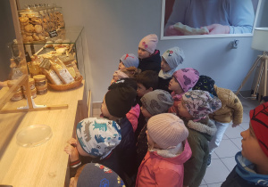 dzieci stoją przed ladą sklepową i przyglądają się ciasteczkom w słoikach
