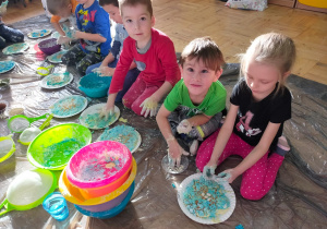 dzieci ozdabiają placki z niebieskiego ciasta, leżące na papierowych talerzykach