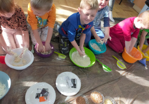 dzieci w miskach ugniatają przesianą mąkę zmieszaną z wodą