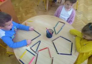 dzieci przy stoliku układają wzory z kolorowych kredek