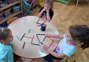 dzieci przy stoliku układają wzory z kolorowych kredek