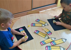 chłopcy przy stoliku składają imienne kredki z literami