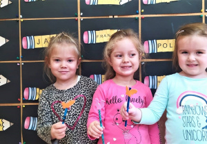 dziewczynki z grupy VIII z kredką ołówkową na tle prac plastycznych - kredek z imionami dzieci