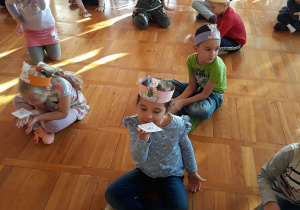 misiowa zabawa oddechowa - dzieci w opaskach z misiem na głowie siedzą skrzyżnie, dmuchają na karteczkę umieszczoną na dłoni