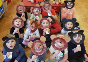 dzieci z grupy VI z pomalowanymi twarzami pozują do zdjęcia, wkładając swoje twarze w brązowe i czarne obręcze z uszami wykonane z papierowych talerzyków
