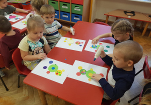 dzieci przy stolikach naklejają kolorowe koła na białe kartki tak aby powstał kolorowy miś