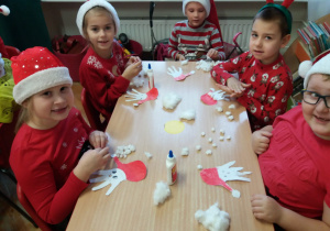 dzieci przy stoliku robią postać Mikołaja z odrysowanej, wyciętej i pokolorowanej dłoni
