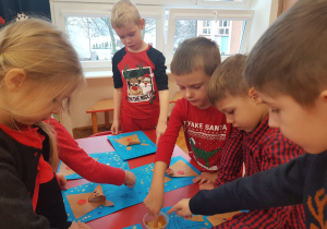dzieci przy stoliku stemplują palcem śnieg na kartce z reniferem