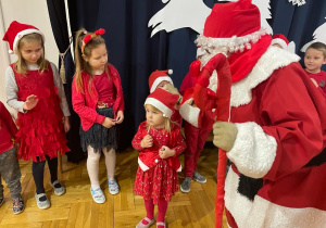 Mikołaj stoi wśród dzieci ubranych na czerwono