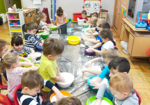 dzieci przy długim stoliku ugniatają ciasto z masy solnej w swoich miskach