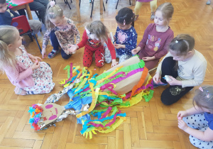 dziewczynki doklejają kolorowe kwiatki na sukienkę marzanny leżącej na podłodze