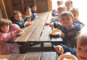 dzieci przy drewnianych stołach jedzą zupę pomidorową
