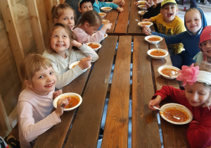 dzieci przy drewnianych stołach jedzą zupę pomidorową