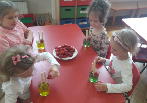 dziewczynki przygotowują deser dla mamy, do galaretki z rurkami dokładają truskawki