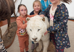 dziewczynki głaszczą wypchane zwierzę - białego lwa