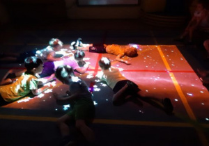 ciemno, dzieci leżą na brzuchach w świetle, w kształcie gwiazd z FUN FLOOR