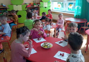 dzieci siedzą przy okrągłych, czerwonych stolikach podczas poczęstunku