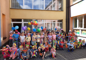 dzieci kolorowo ubrane pozują do zdjęcia z balonami, hulajnogami, kolorowymi wstążkami
