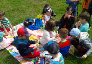 dzieci w ogrodzie przedszkolnym siedzą na macie podczas pikniku