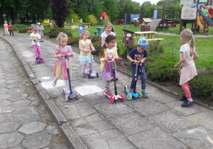 w ogrodzie przedszkolnym dzieci jeżdżą na hulajnogach