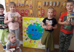 dzieci 5 i 6 letnie nagrodzone w konkursie plastycznym - stoją w sali, przed tablicą z plakatem - kulą ziemską a wokół niej dzieci oraz maskami indiańskimi wykonanymi z rolek papieru i plasteliny