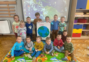 dzieci z gr VII z plakatem - Ziemia pomalowana niebieską farbą i zielonymi kulkami bibuły naklejonymi na kontury lądów