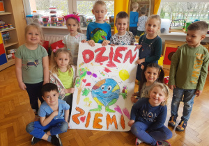 dzieci z grupy VI z plakatem - ZIemia a wokół serca, motyle, kwiaty, słońce i ptaki oraz napis Dzień Ziemi