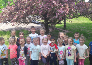 dzieci pozują do zdjęcia pod kwitnącym na różowo drzewem