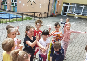 dzieci na tarasie przedszkolnym bawią się wśród baniek mydlanych