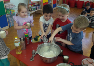 dzieci wysypują do dużej, srebrnej miski mąkę ze szklanek